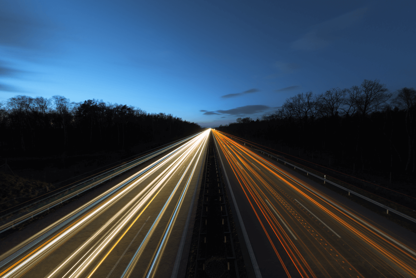 Orange and White light beams across the highway in a dark road and blue clear skies.