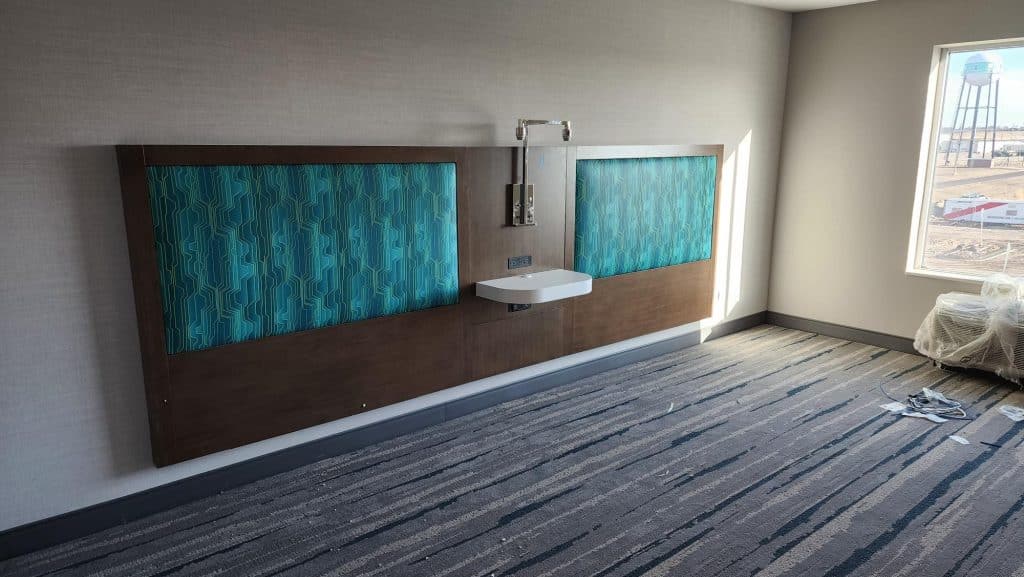Hotel room head board upholstered with fixture and center table. It shows the beginning of an installation of hotel rooms.